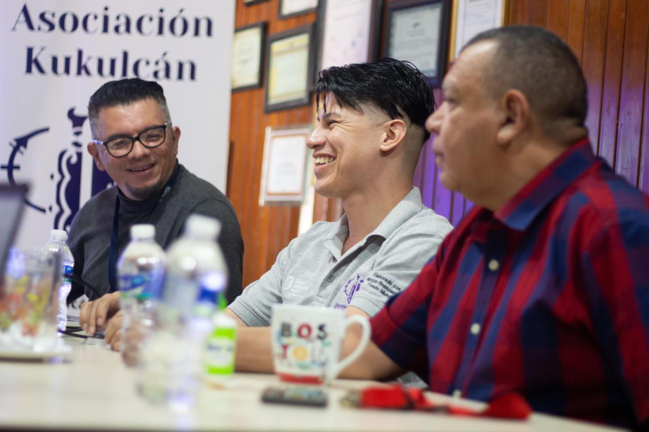 Tres hombres jóvenes sonrien durante un diálogo en sala de conferencias de su organización