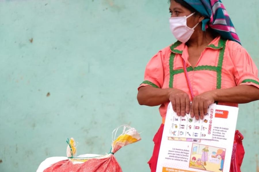 Mujer indígene junto a saco de alimentos y cartilla informativa de COVID-19
