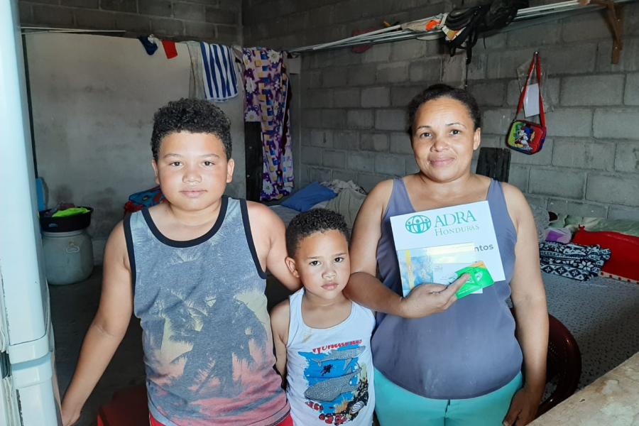Madre y sus dos hijos mostrando la tarjeta prepago de supermercado recibida por ADRA Honduras
