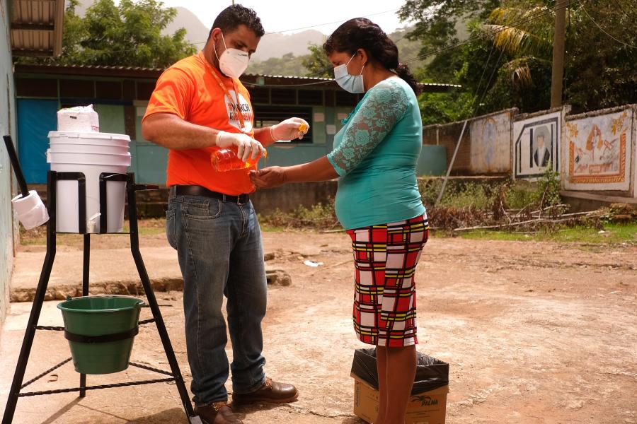 Funcionario Care Honduras coloca jabón a mujer frente a estación de lavado de manos instalada en la comunidad