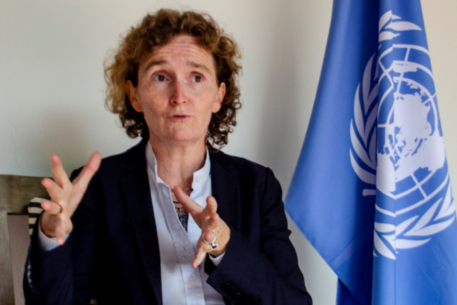 Alice Shackelford hablando con la prensa frente a bandera de Naciones Unidas