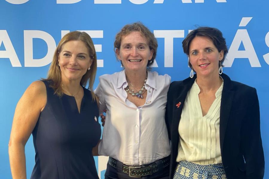 Luisa Cabal, Marie Engel de ONU SIda, y Alice Shackelford de ONU Honduras posan para una fotografía sonriendo frente a una pared azul