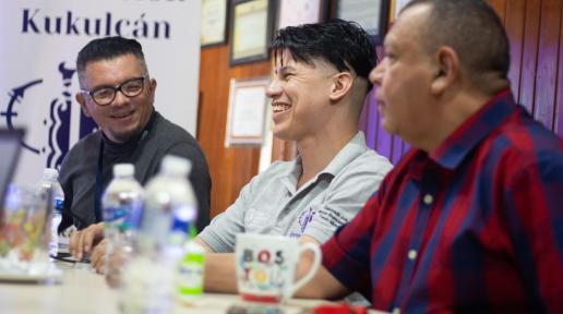 Tres hombres jóvenes sonrien durante un diálogo en sala de conferencias de su organización