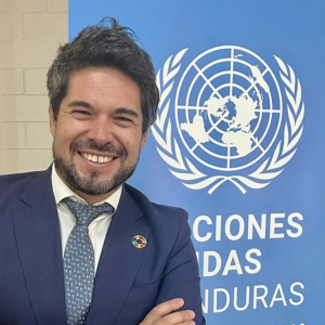 Nahuel viendo a cámara frente a un banner azul con el logo de Naciones Unidas Honduras.