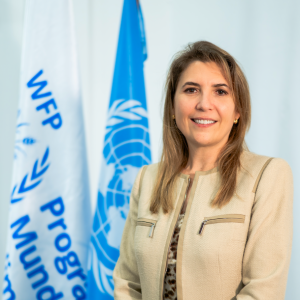 Stephanie sonríe usando un saco café, frente a las banderas del PMA y Naciones Unidas
