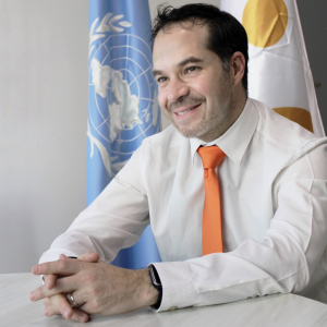 Ivan, hombre blanco de pelo oscuro sentado frente a una bandera de la ONU y una de UNFPA.